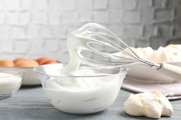 Whisk with whipped cream and other ingredients on gray wooden table. Cooking meringue cookies