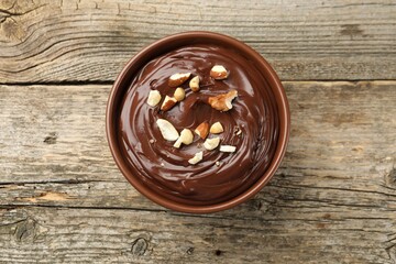 Delicious chocolate pudding with nuts in bowl on wooden table, top view