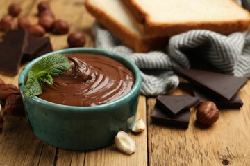 Tasty hazelnut spread with mint, chocolate pieces and nuts on wooden table, closeup