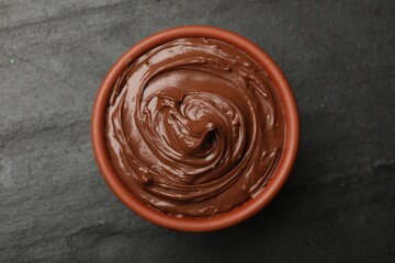 Tasty chocolate spread in bowl on black table, top view