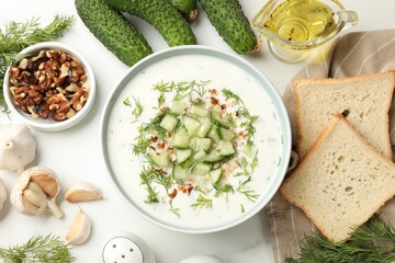 Tasty cucumber soup with dill and nuts in bowl among products on white table, flat lay