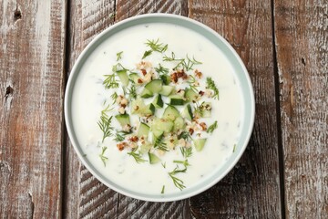 Tasty cucumber soup with dill and nuts in bowl on wooden table, top view