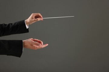 Professional conductor with baton on grey background, closeup. Space for text