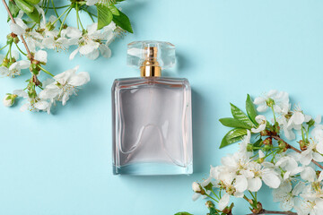 Bottle of aromatic perfume and twigs with beautiful flowers on light blue background, flat lay