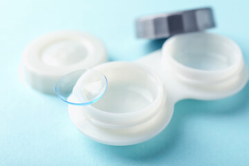 Contact lenses and case on light blue background, closeup
