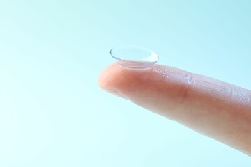 Woman with contact lens on light blue background, closeup. Space for text