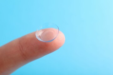 Woman with contact lens on light blue background, closeup. Space for text