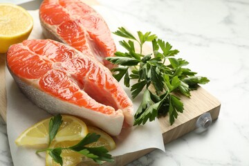 Seafood. Fresh raw salmon steaks, parsley and pieces of lemon on white marble table, closeup