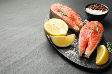Seafood. Salmon steaks, spices and lemon on black textured table, closeup. Space for text
