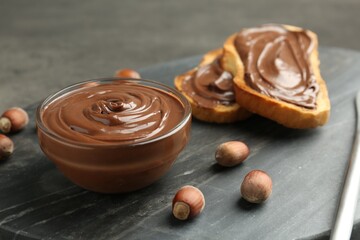 Tasty chocolate spread, toasts and hazelnuts on gray table, closeup