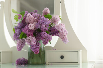 Beautiful lilac flowers in vase on dressing table indoors