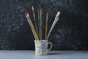 Dirty paintbrushes in cup on grey table