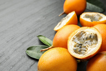 Ripe passion fruits and green leaves on black table, closeup. Space for text