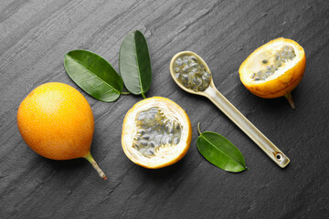 Ripe passion fruits, seeds and green leaves on black table, flat lay