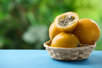 Ripe passion fruits in wicker basket on light blue wooden table outdoors, closeup. Space for text