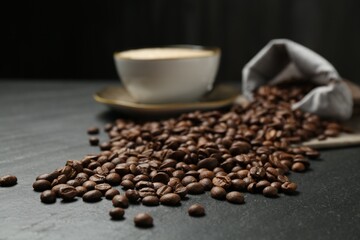 Aromatic coffee beans and hot drink on black table, closeup