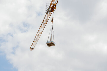 A tall crane on a construction site, blue sky. Construction crane in the sky. Yellow crane tower lifting up