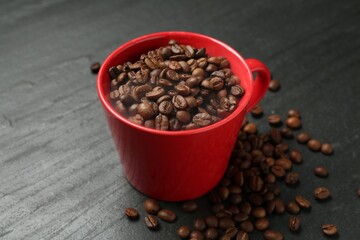 Aromatic coffee beans in cup on black table, closeup