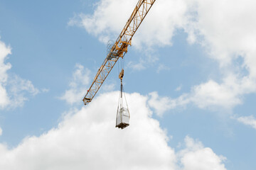 A tall crane on a construction site, blue sky. Construction crane in the sky. Yellow crane tower lifting up