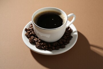 Aromatic coffee in cup and beans on beige background, closeup