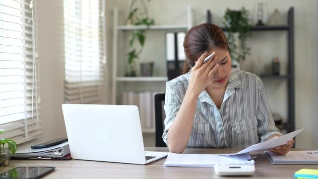 Young Businesswoman is seriously stressed and upset working on tablet and document paperwork , headache due to office syndrome on laptop and paperwork in the office.
