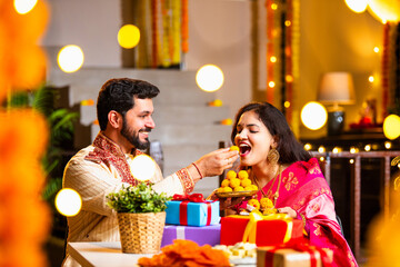 Indian Couple Sitting Indoors Enjoying Laddoo Together During Diwali Night Celebration