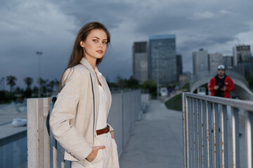 Confident woman in neutral suit posing against urban cityscape background during overcast day,...