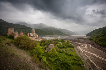 Ancient fortress beside a winding river surrounded by mountains under a dramatic sky