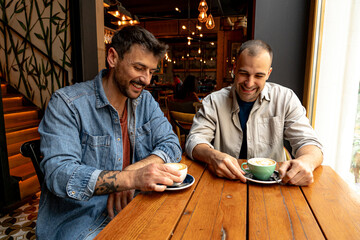 Two men are sharing a moment of laughter and connection over coffee in a warm and inviting cafe