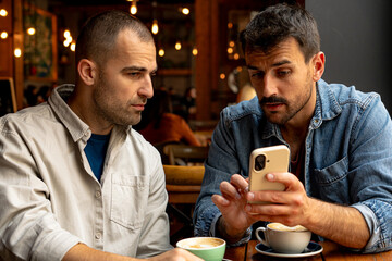 Two businessmen looking at smartphone and drinking cappuccino, during a business meeting in a cafe