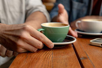 Business partners engaging in discussion over coffee, holding cappuccino cups while seated at a wooden table in a cozy cafe setting