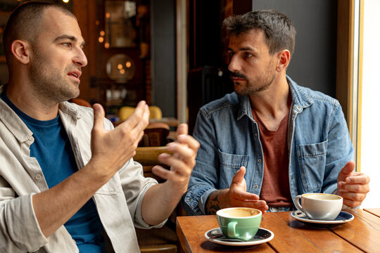 Two men sitting together at a table in a cafe, enjoying coffee and engaging in animated gestures while discussing various topics