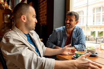 Two male friends are catching up over coffee in a cozy cafe, engaging in lively conversation and...