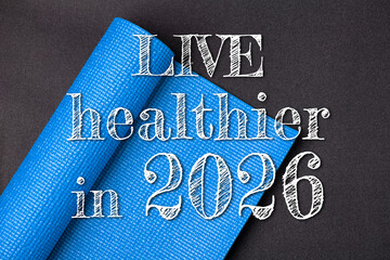 New year 2026 resolutions healthy lifestyle and sport. Live healthier in 2026. Motivation sport goals 2026 with sport equipment blue yoga mat on black background