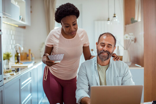 Happy couple spending quality time together in modern kitchen with laptop and breakfast