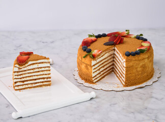 Layered Medovik Honey Cake with strawberry and blueberry slice isolated on grey background side...