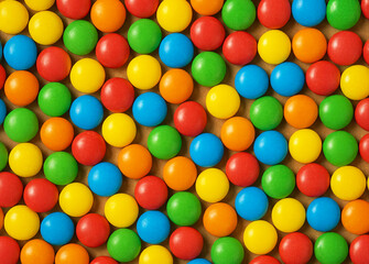 Obraz premium Colorful chocolate candies in red, yellow, green, blue, and orange arranged in a seamless pattern. Fun and vibrant background for sweets, parties, or advertising.