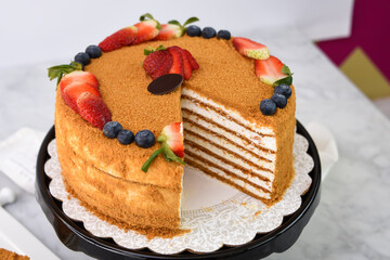 Elegant Medovik Honey Cake decorated with fresh strawberries and blueberries and displayed on a...