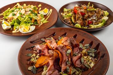 Traditional Eastern European cuisine served on rustic clay plates. A variety of homemade dishes including meat, potatoes, pancakes, dumplings and grilled vegetables, on a rustic background, top view.