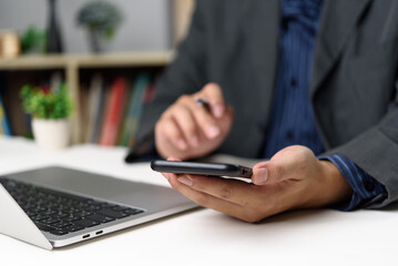 Businessman using smartphone and laptop in modern office, representing digital workflow and mobile...