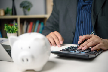 Businessman calculating financial plans with calculator and piggy bank, budget planning.Office...