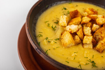 Creamy pea soup with golden croutons and fresh dill served in a clay bowl. Traditional homemade comfort food, top view, rustic style