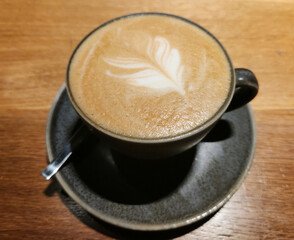 Latte in a ceramic cup with a leaf design, Hot coffee on wooden surface