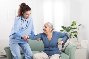 Caring smiling nurse or doctor taking care of elderly woman patient while helping her walking with...