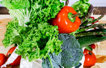 Linen eco shopper bag with fresh food, vegetables, salad and asparagus on wooden table in cozy modern kitchen. Products for healthy cooking close-up