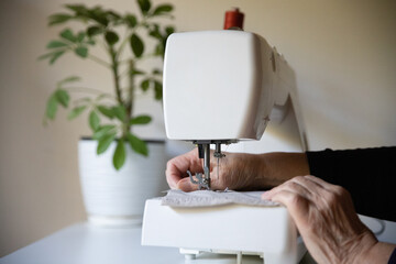Hands sewing against the background of shvetka seamstress old grandmother production