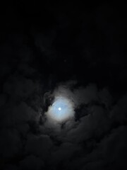 A mystical scene featuring a glowing full moon peeking through soft, wispy clouds against a dark night sky. The ethereal glow of the moon contrasts beautifully with the cloudy atmosphere, evoking feel
