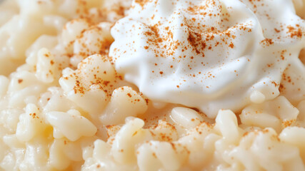 An overhead, close-up shot of a bowl of traditional rice pudding, topped with a sprinkle of cinnamon and a dollop of whipped cream.