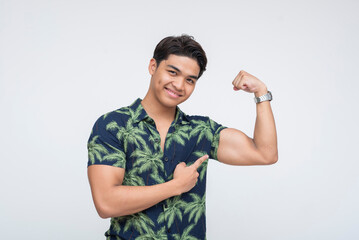 Portrait of a smiling young Southeast Asian man confidently flexing his arm and pointing to his...