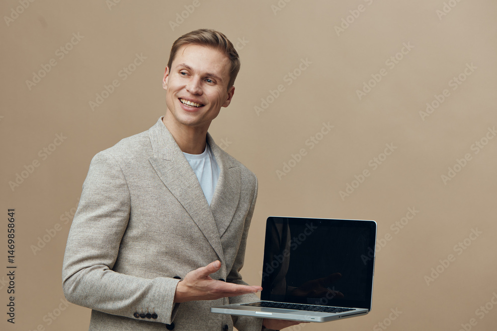 Poster smiling happy young man holding open laptop computer in hand posing isolated on beige background stu